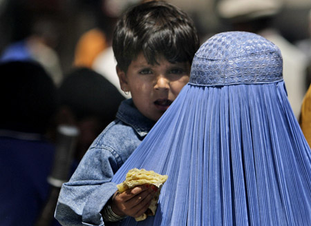 An Afghan girl holds bread in her hand as she is carried by her mother  in Kabul. The International Conference in Support of Afghanistan in Paris tomorrow represents an opportunity for the United States to make good on its pledges to the country. (AP/Rafiq Maqbool)