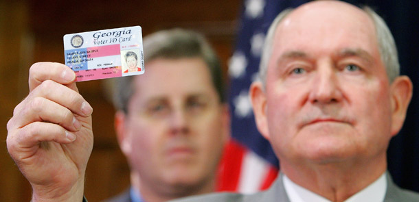 Georgia Gov. Sonny Perdue holds up a proposed voter ID. Regulations such as laws requiring ID to vote, apply for jobs, open a bank account, and fly on a plane are squeezing Americans who find themselves on the wrong side of the ID Divide. (AP/Ric Feld)