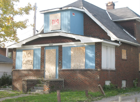 A vacant home in Cleveland has been boarded up, and writing indicates that the house has been stripped of copper. (Flickr/edkohler)