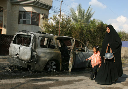 An Iraqi woman and her daughter walk by a car damaged in a bombing in the eastern Baghdad neighborhood of Mashtal. Smaller, more targeted bombings have replaced large-scale ones recently in Iraq. (AP/Hadi Mizban)