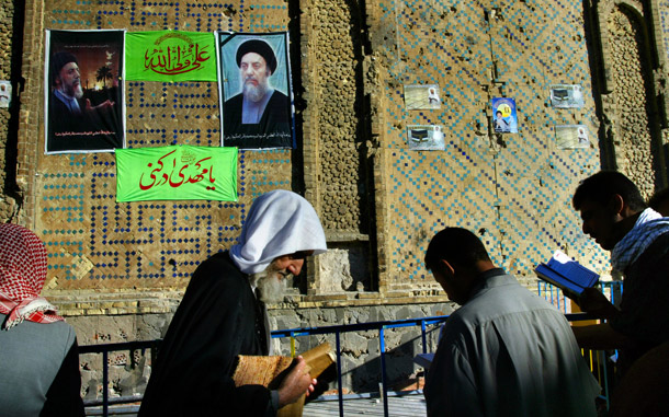 Shia Muslims pray near the poster-clad compound wall of the Imam Ali Tomb. (AP/Brennan Linsley)