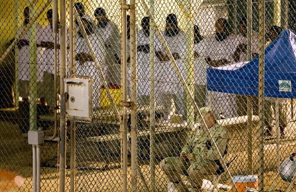 Detainees at the prison at Guantanamo Bay participate in the morning prayer, as a U.S. guard watches nearby. (AP/Brennan Linsley)