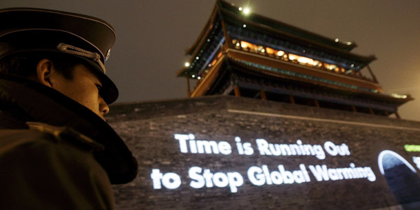 A security guard looks on as a slogan is projected onto Yongdingmen Gate in Beijing, China. The Chinese have recognized that it’s climate inaction—not climate legislation—that will lead to its own economic undoing. (AP/Greg Baker)