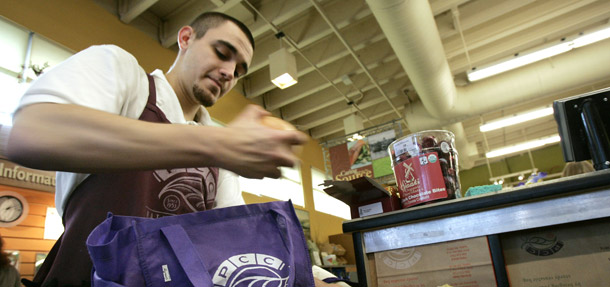 An employee at a PCC Natural Market in Seattle, WA bags a customer's groceries into a cloth bag. On August 18 Seattle will vote on a plastic bag fee modeled after Ireland's successful PlasTax fee. (AP/Elaine Thompson)