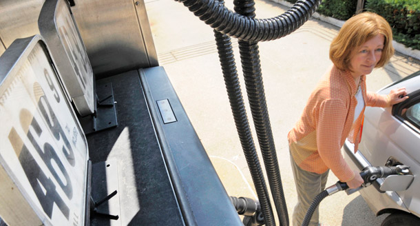 A woman pumps gas to the right of a sign for self-serve unleaded in Lexington, Massachusetts. (AP/Lisa Poole)