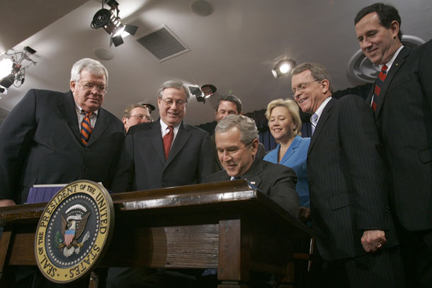 Former President George W. Bush, seated, signs the Tax Relief and Health Care Act of 2006 in the Eisenhower Executive Office Building in Washington. The policies of the Bush administration, which included tax cuts during a time of war and a floundering economy, are the primary source of the current deficits. (AP/Haraz N. Ghanbari)