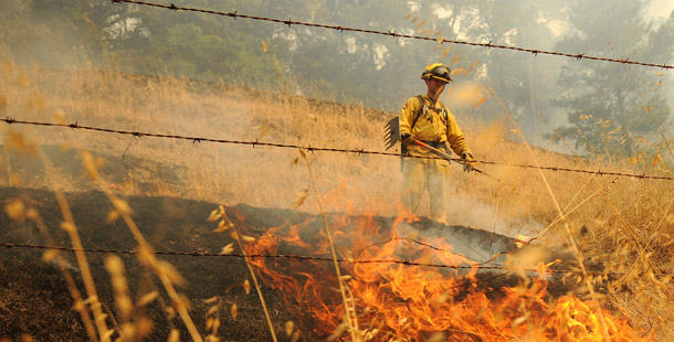 A firefighter battles a wildfire as it threatens to jump a road in unincorporated Santa Cruz County, CA, on August 14, 2009. (AP/Noah Berger)