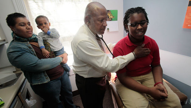 Dr. Michael Lenoir examines Ebony Jones, 13, as her mother Daaiyah Shabazz and brother Dante Jones look on. (AP/Marcio Jose Sanchez)