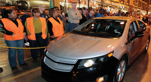 Workers in a Detroit, Michigan plant stand by a newly produced Chevy Volt plug-in hybrid electric vehicle. (Rebecca Cook)