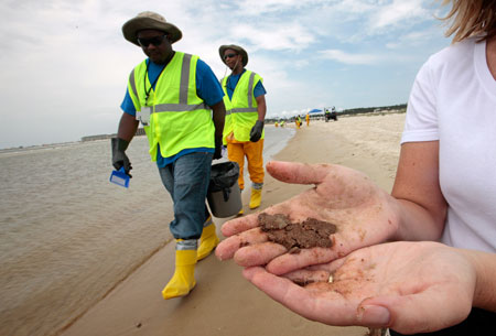 Clean-up workers walk along the beach; a women holds clumps of sandy oil that has washed up on Dauphin Island, Alabama. (AP/Dave Martin)