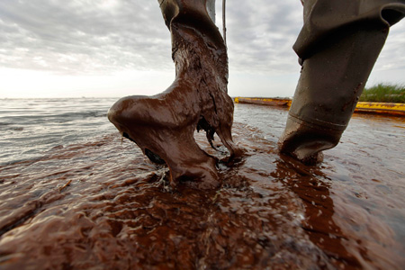 Plaquemines Parish coastal zone director P.J. Hahn lifts his boot out of thick, beached oil at Queen Bess Island in Barataria Bay, just off the Gulf of Mexico in Plaquemines Parish, Louisiana. (AP/Gerald Herbert)