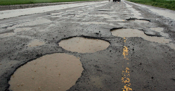 Potholes are visible on a farming back road in Tulare, California. More than 146,000 of the 600,000 bridges in this country are failing, and nearly 800,000 miles of our roadways are in unacceptably poor condition, contributing to accidents and congestion. (AP/Gary Kazanjian)