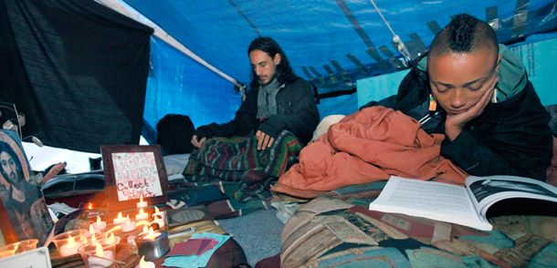 Occupy Boston resident Khepe-Ra Maat-Het-Heru, of New Bedford, Massachusetts, reads at right, while Ben Lewis of Sydney, Australia, prays in the faith and worship tent in downtown Boston. One of the most illustrative images of interfaith partnerships is the “faith and spirituality tent” built by faith leaders in Occupy Boston. (AP/Elise Amendola)