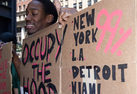 Un hombre levanta un letrero de “Occupy the Hood” (Ocupar el Barrio). Los esfuerzos de esta red están diversificando el movimiento de “Ocupar Wall Street”, y las personas de color ven los vínculos entre sus intereses y los mensajes del movimiento. (Flickr/<a href=