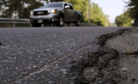 A truck drives past a crumbling road in Durham, Maine. The new federal highway bill takes some steps to improve our infrastructure, but it doesn't go far enough to meets the transportation needs of a 21st century America. (AP/Pat Wellenbach)