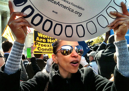 A girl waves a sign at a rally supporting Obamacare. The law offers many benefits for young people of color including a provision that lets young people stay on their parents' insurance plan until they're 26. (Flickr/<a href=http://www.flickr.com/photos/ladawnaspics/7029979945/