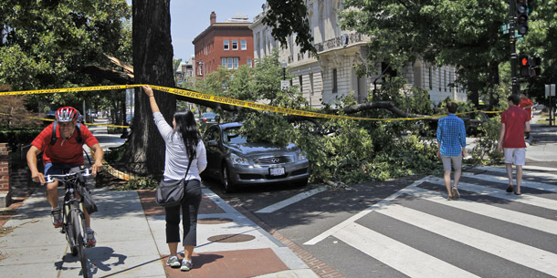 A pedestrian helps a bicyclist navigate a sidewalk blocked by a fallen tree that also damaged a parked vehicle in the Dupont Circle neighborhood of Washington, D.C., on June 30, 2012. A storm barreled through the Midwest and Mid-Atlantic regions last Friday, knocking out power for 2 million people.  (AP/Pablo Martinez Monsivais)