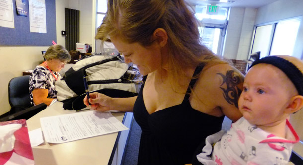 Laura Fritz, 27, left, with her daughter Adalade Goudeseune, fills out a form at the Jefferson Action Center, an assistance center in the Denver suburb of Lakewood. Many Americans like Fritz who once enjoyed middle-class status are being squeezed out due to policies enriching a wealthy ruling class.<br /> (AP/Kristen Wyatt)