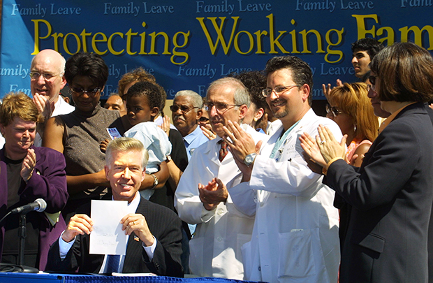 Then-Gov. Gray Davis (D-CA) holds up the paid family leave bill, Senate Bill 1661, after signing it during a news conference at the University of California, Los Angeles, Monday, September 23, 2002, in the Westwood area of Los Angeles. (AP/Lee Celano)