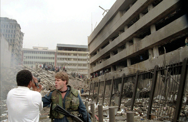 A security guard instructs a cameraman to move back following a bombing that heavily damaged the U.S. Embassy in Nairobi, Kenya, right, Friday, August 7, 1998. Nine Americans serving in the embassy were killed in the bombing, including Deputy Chief of Mission Julian Bartley. (AP/Sayyid Azim)