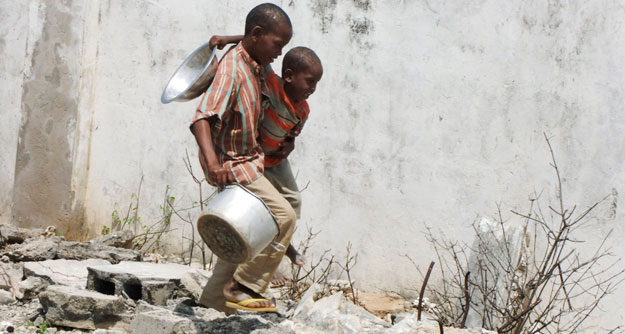 Two Somali children carrying a bowl and a pot walk to a food distribution center. As the election gets closer, the media must force politicians to discuss poverty and hunger, both in America and abroad. (AP/Farah Abdi Warsameh)