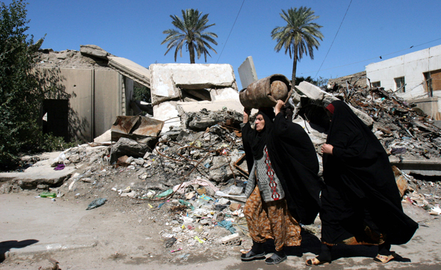 Iraqi women pass by a house destroyed during air campaign at early stages of war, in Baghdad, Iraq, March 18, 2007, ahead of the fourth anniversary of the U.S. invasion on Iraq. The 10th anniversary of the invasion is later this month. (AP/Samir Mizban)