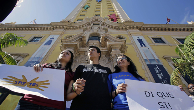 Federico Paseiro, center, his mother Patricia Sosa, right, both undocumented immigrants of Argentina, and his girlfriend Daysis Moraga, an immigration activist, left, hold signs in front of the Freedom Tower in downtown Miami, Monday, January 28, 2013. (AP/Alan Diaz)