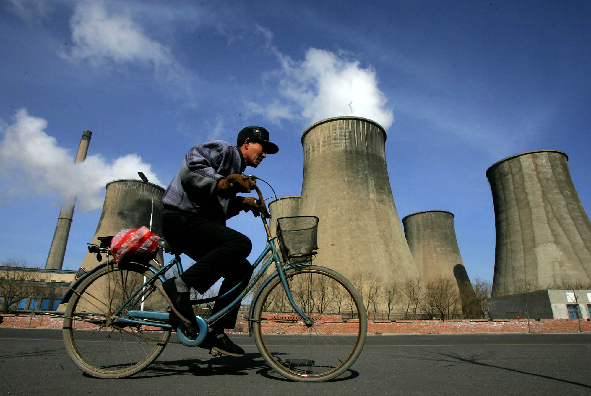 A man cycles past cooling towers of the coal powered Fuxin Electricity Plant in Fuxin, China. (AP/Greg Baker)
