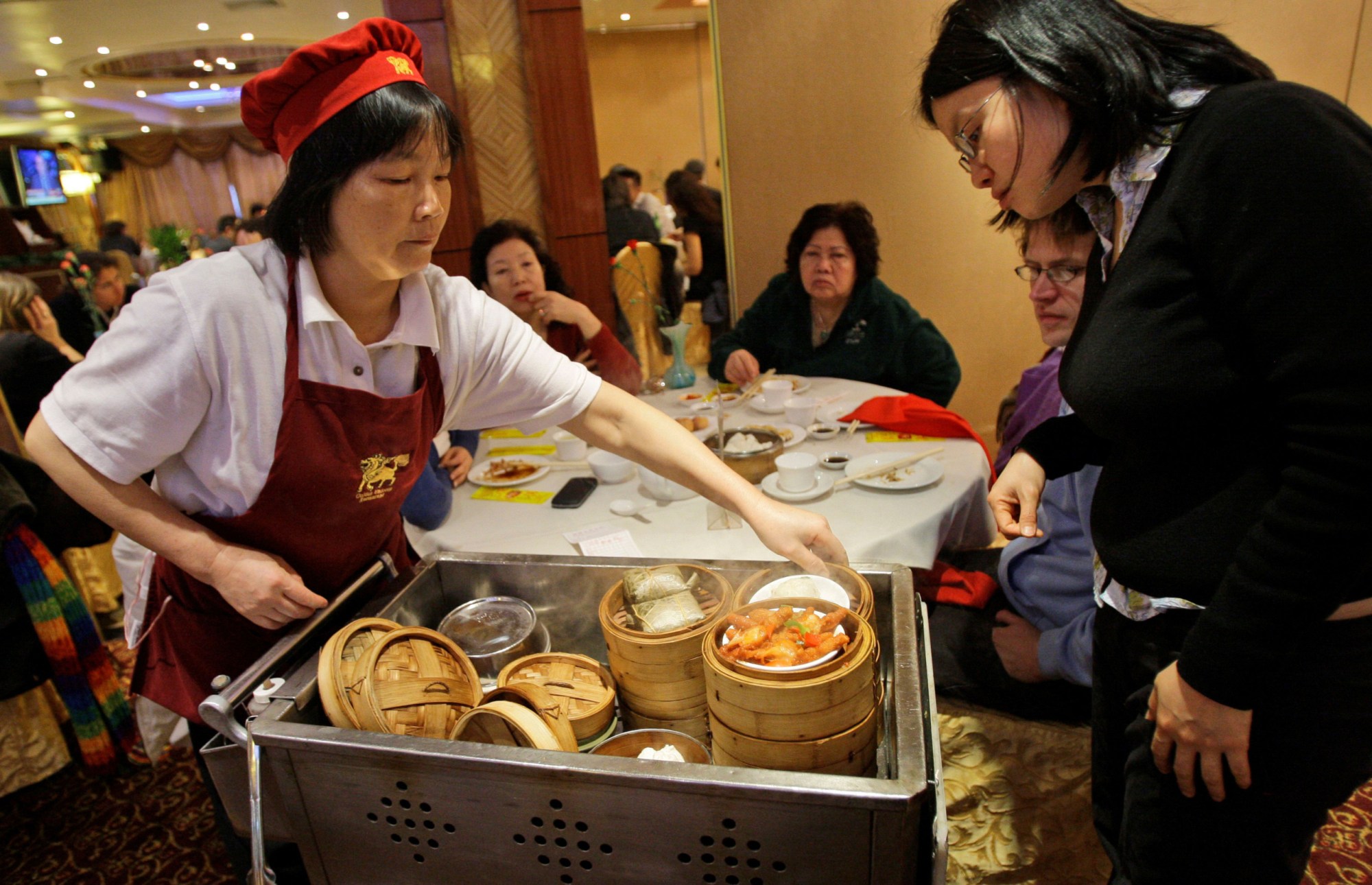 A waitress serves steamy containers of dim sum at the Golden Unicorn restaurant in Chinatown in New York. Asian American women earn significantly less than their male counterparts. (AP/ Kathy Willens)
