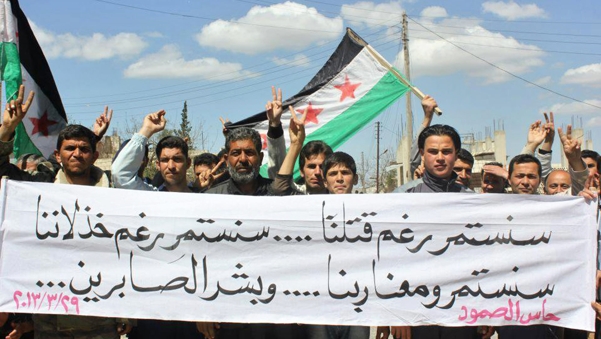 Anti-Syrian regime protesters hold a banner and Syrian revolution flags during a demonstration in the town of Haas in the northwestern province of Idlib, Syria. (AP)