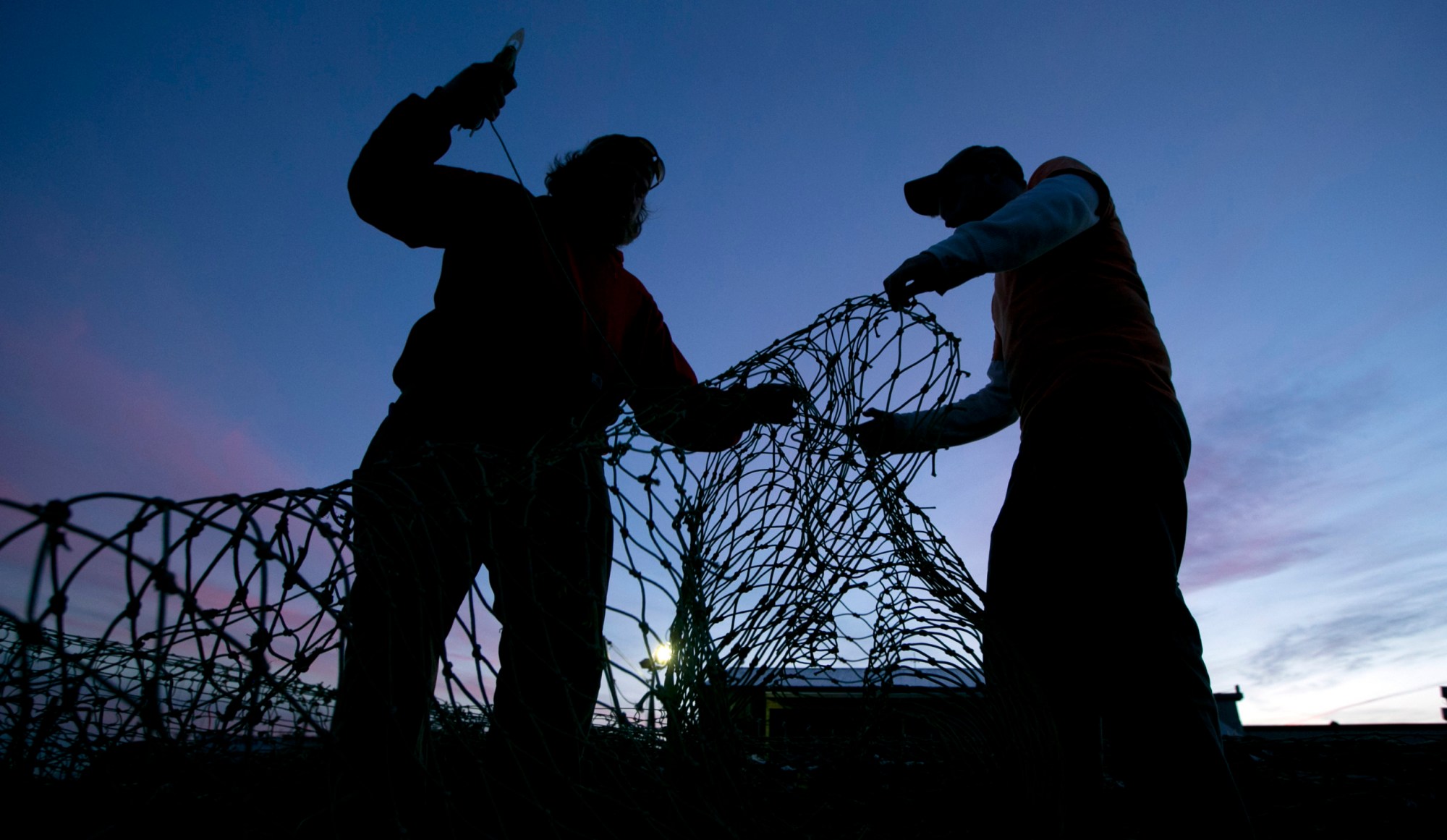 Fishermen Lucas Dewildt and Dillon Robbins mend groundfishing nets in Portland, Maine. (AP/Robert F. Bukaty)