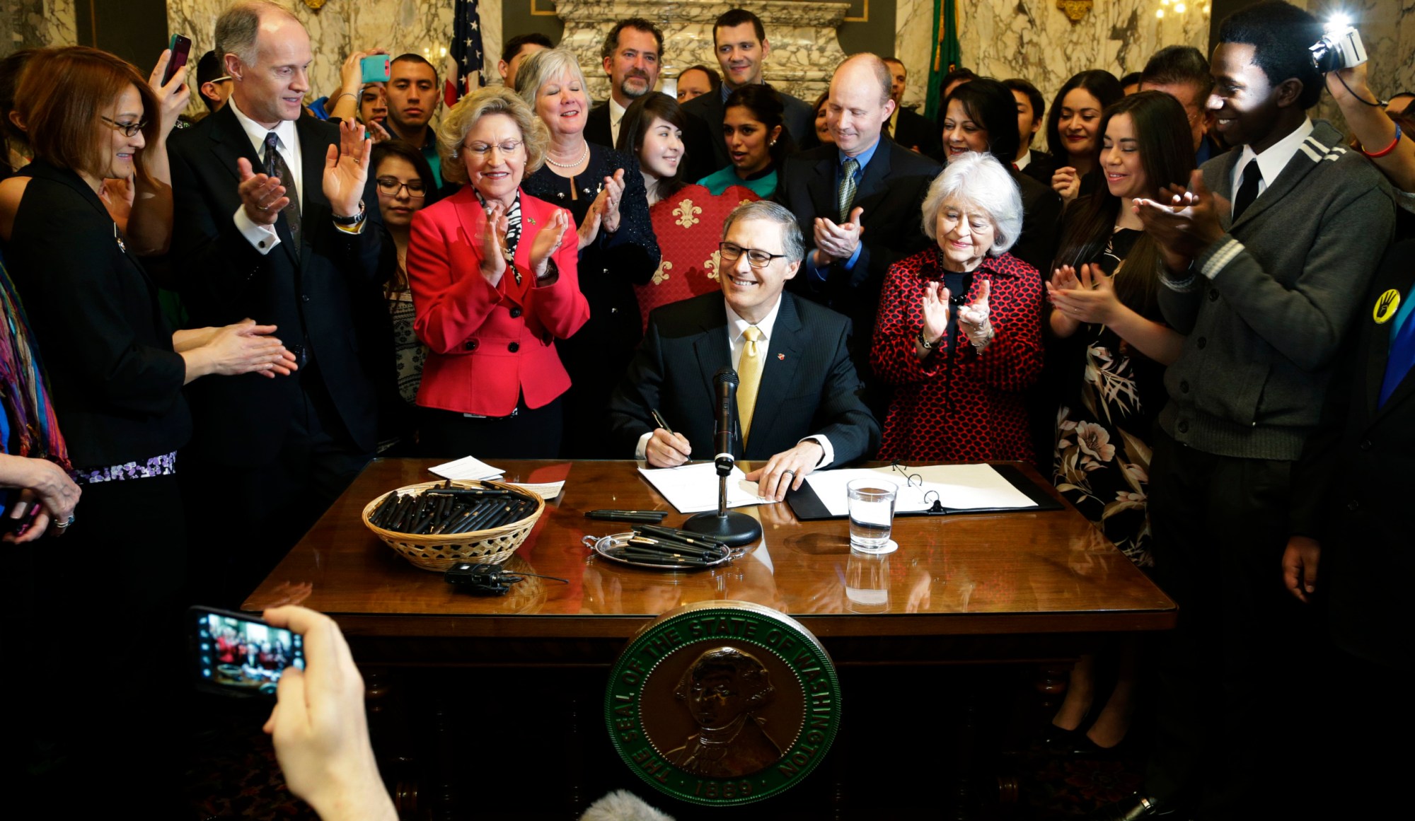 Washington Gov. Jay Inslee (D) signs a measure into law that expands state financial aid to undocumented students. (AP/Ted S. Warren)