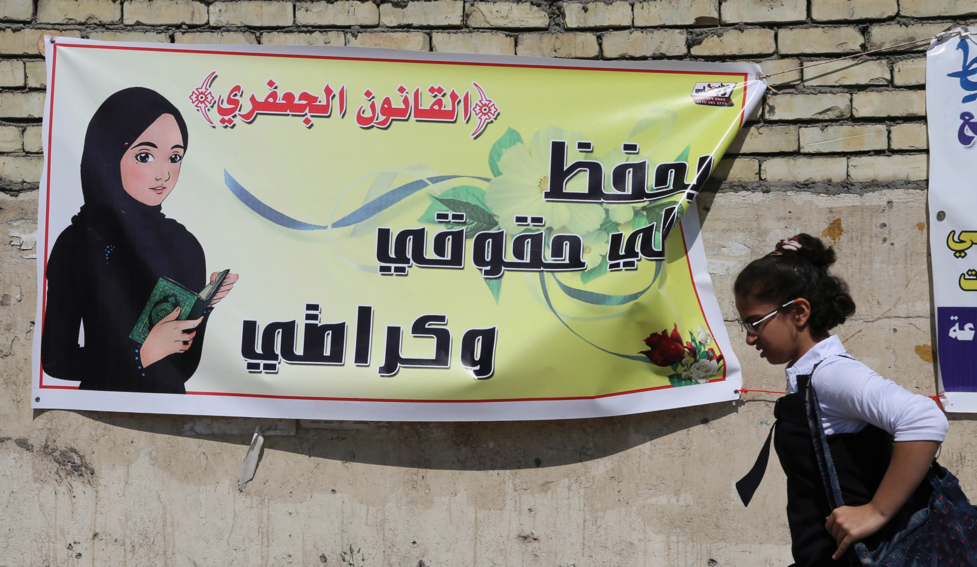 A schoolgirl passes a banner for the Jaafari personal status law in Baghdad. The Arabic on the banner reads, 