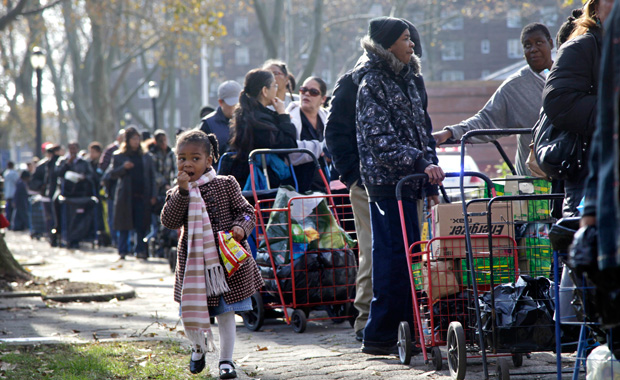Two weeks after Superstorm Sandy, Amber Whichard, 3, walks next to a line of people waiting to receive supplies donated to the victims of the hurricane at the Red Hook Houses in the Brooklyn borough of New York, November, 12, 2012. (AP/Seth Wenig)