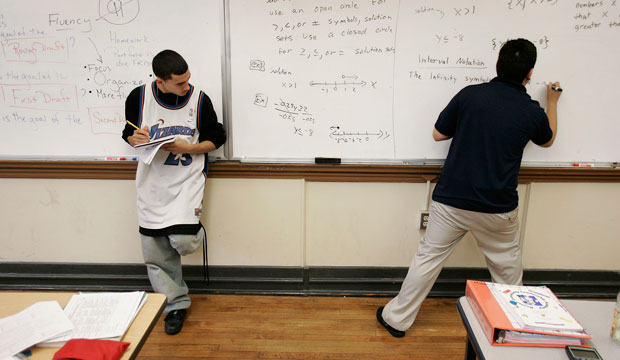 Jimmy Guevara, 17, left, stands next to the board taking notes during his 10th-grade math class as teacher Sammy Gutierrez works a problem at the Boston Community Leadership Academy pilot high school in the Brighton section of Boston, Massachusetts. (AP/Stephan Savoia)