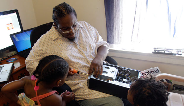 Carl Tabb, a 36-year-old father of 10 who hopes to earn a bachelor's degree in information technology from the University of Phoenix, takes apart a computer as his children watch. (AP/Jeff Roberson)