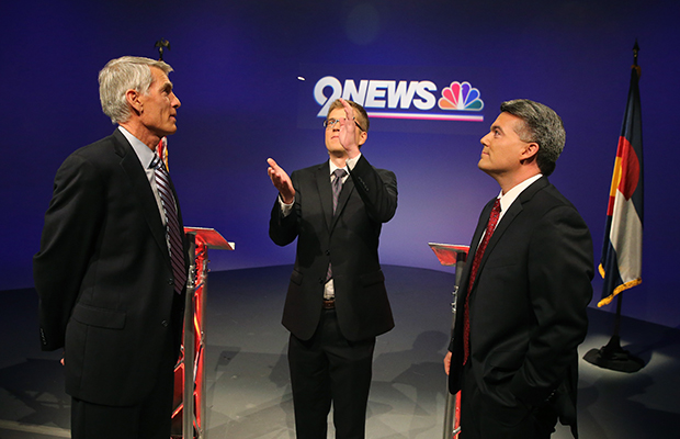 Incumbent Sen. Mark Udall (D-CO) and his opponent Rep. Cory Gardner (R-CO), right, watch a coin flip by moderator Brandon Rittiman to see who gets the first question during their final pre-election televised debate at 9News in Denver, October 15, 2014. (AP/Brennan Linsley)