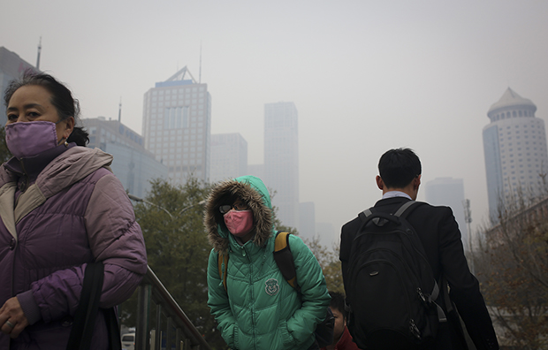 People wearing masks to protect themselves from pollutants walk on a pedestrian overhead bridge as city skylines are shrouded with haze in Beijing, China, Wednesday, November 19, 2014. (AP/Andy Wong)