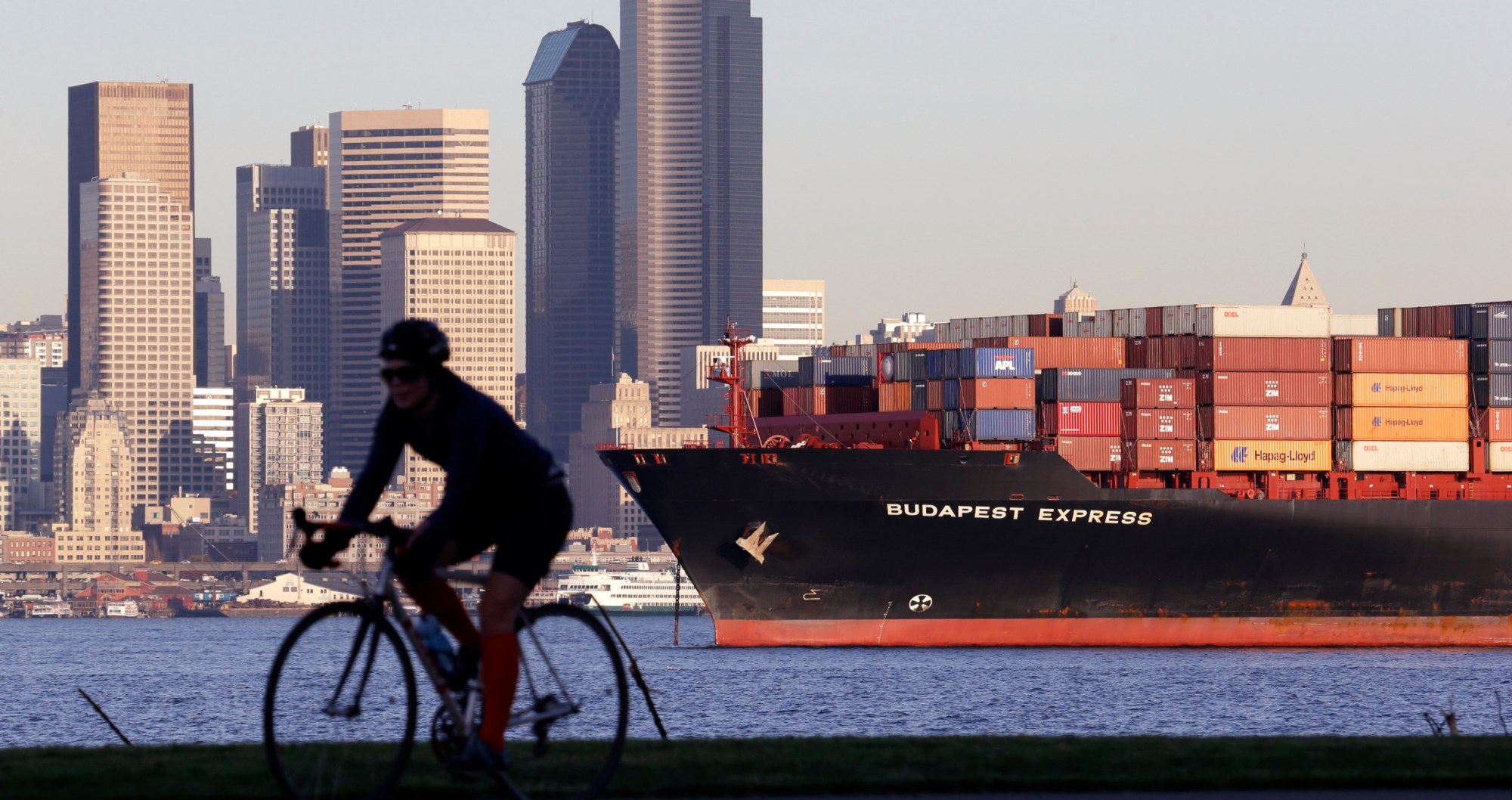 A bicyclist rides near a container ship anchored in Elliott Bay near downtown Seattle. (AP/Elaine Thompson)
