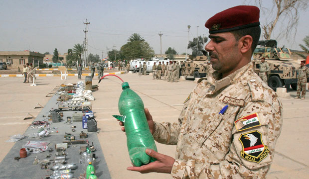 An Iraqi soldier carries a beverage bottle used as an IED that was seized by Iraqi security forces in Baghdad's Abu Ghraib suburb in 2010. (AP/Loay Hameed)