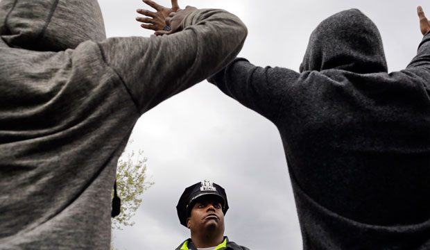 A Baltimore police officer stands guard outside of the Western District police station as men hold their hands up in protest during a march for Freddie Gray on April 22, 2015. (AP/Patrick Semansky)