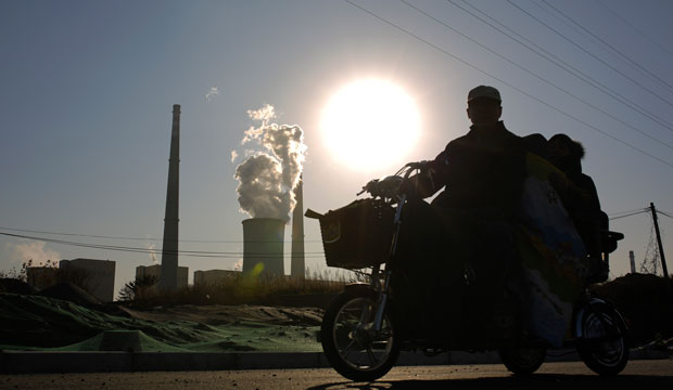 A family riding an electric tricycle bike is silhouetted against the sun setting on a coal-fired power plant in Beijing, China, November 2014. (AP/Andy Wong)