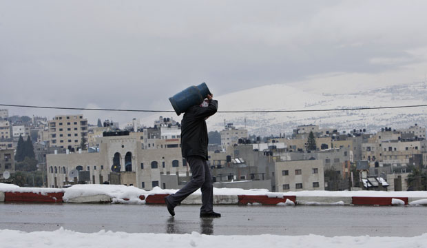 A Palestinian man carries a gas tank in the West Bank town of Nablus in December 2013. (AP/Nasser Ishtayeh)