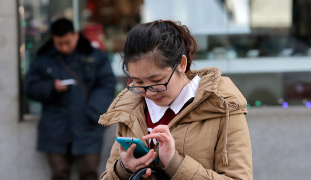 Chinese people check on their smartphones on a street in Beijing on February 16, 2015. (AP/Andy Wong)