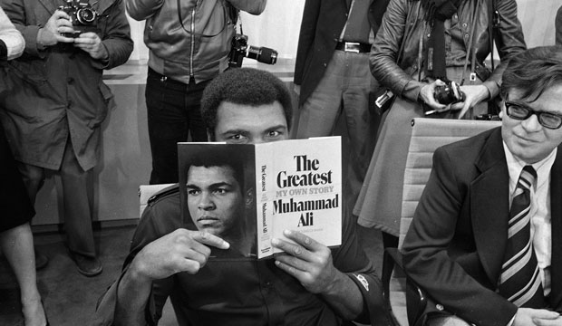 Muhammad Ali peers over a copy of his autobiography, 