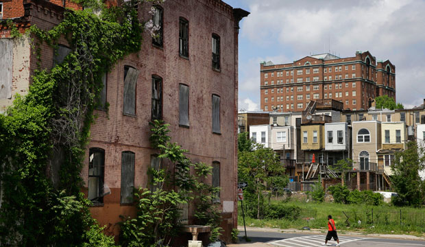 A man walks past a blighted building in the Penn-North neighborhood of Baltimore, with a residential tower in the Reservoir Hill neighborhood in the background at top right, on May 9, 2015. (AP/Patrick Semansky)