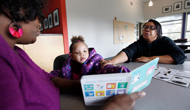 Taliyah Garrett reads as her mother, Tawana Brooks, follows along with coordinator Jazmyn Scott after Taliyah during a Parent Child Home Program visit in Seattle, December 2011. (AP/Elaine Thompson)