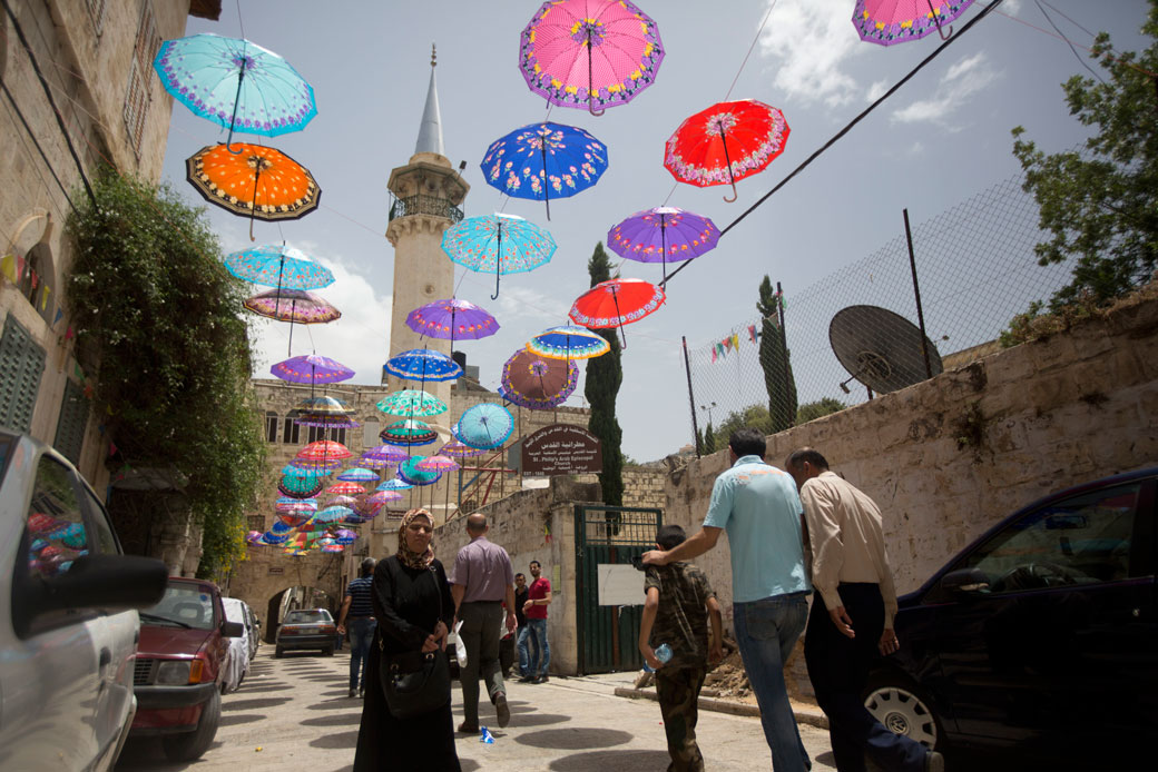 Palestinians walk under show umbrellas used to decorate a street in the Old City of the West Bank town of Nablus, Saturday, June 4, 2016. (AP/Majdi Mohammed)