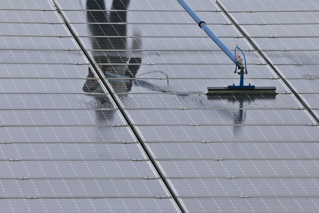 A worker cleans solar collectors on the roof of a farm on May 15, 2014. (AP/Frank Augstein)