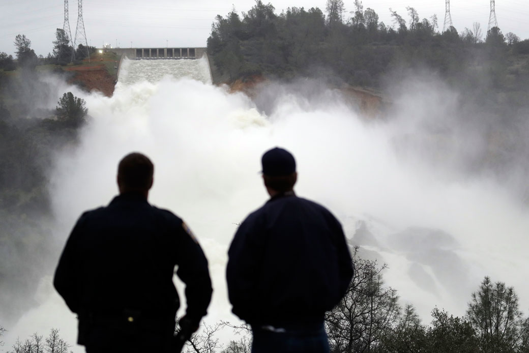 Two men watch as water gushes from the Oroville Dam's main spillway Wednesday, February 15, 2017, in Oroville, California. (AP/Marcio Jose Sanchez)